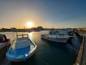 Boats moored in harbor at sunset