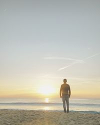 Rear view of men on beach against sky during sunset