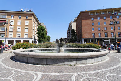 Fountain in front of building against sky on sunny day