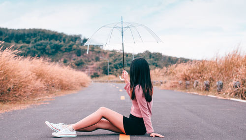 Side view of woman holding umbrella while sitting on road