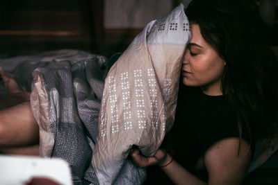 Close-up of young woman holding blanket on bed