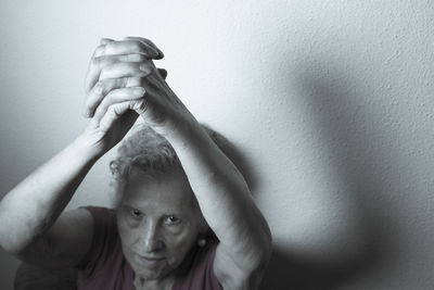 Portrait of senior woman with hands clasped against wall