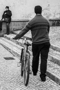 Rear view of man with bicycle on street in city