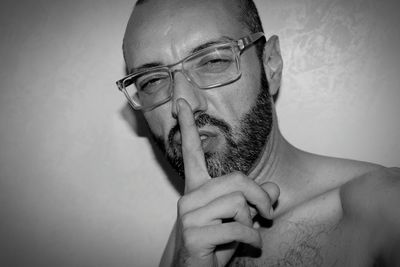 Close-up portrait of bearded man wearing eyeglasses while gesturing finger on lips at home