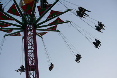 Low angle view of people on chain swing ride against clear sky