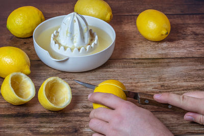 Cropped hands of person cutting lemons by juicer on table