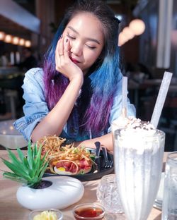 Woman with dyed hair looking at food in restaurant