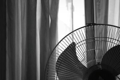 Close-up of cropped electric fan against curtained window