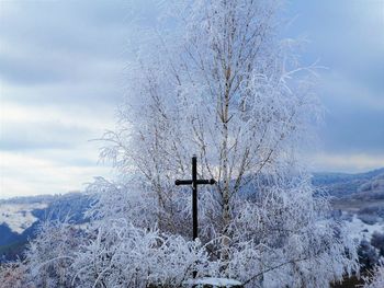 View of cross on snow covered landscape against sky