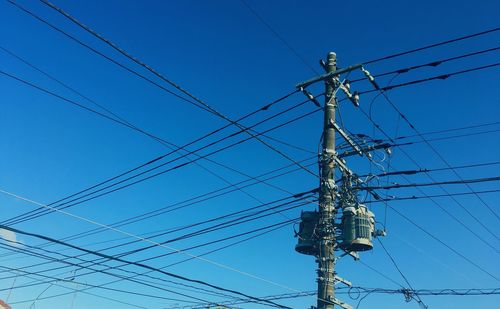 Low angle view of electricity pylon against blue sky