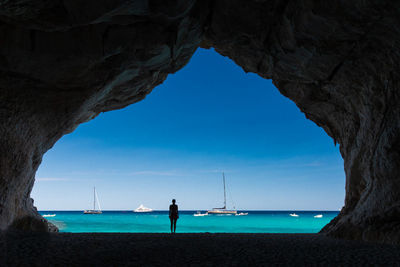 Silhouette woman standing in cave at beach against sea and sky