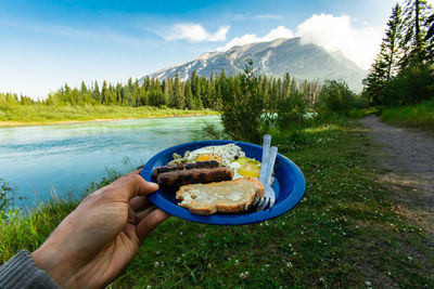 Midsection of person holding ice cream on mountain against sky