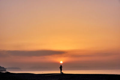 Silhouette woman standing by sea against sky during sunrise