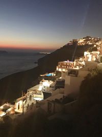 High angle view of illuminated buildings by sea against sky at dusk