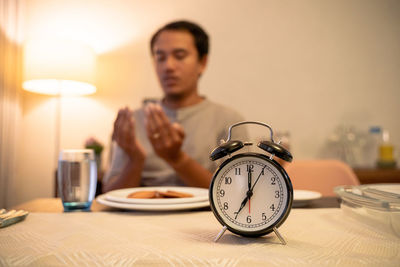 Portrait of young woman with alarm clock on table