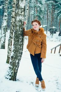 Portrait of young woman standing by trees on snow covered tree