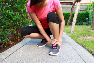 Low section of woman massaging foot while sitting on footpath at park