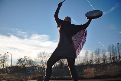 Low angle view of woman holding musical instrument standing against sky