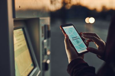 Woman buying ticket at ticket machine paying using mobile payment app on phone. public transport