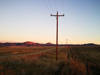 Electric poles on grassy field against clear sky during sunset