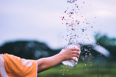 Cropped hand throwing confetti against sky