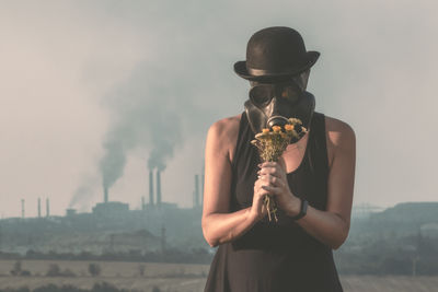 Woman wearing gas mask holding flowers while standing outdoors