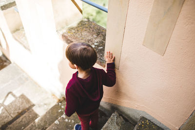 Rear view of boy standing on steps by wall