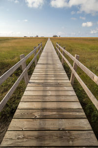 Wooden footbridge leading towards landscape against sky