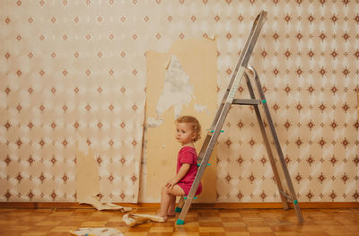 Child tear off the wallpaper from the wall in the room, little mother's helper