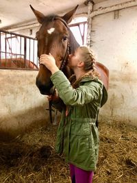 Side view of girl kissing horse standing at barn