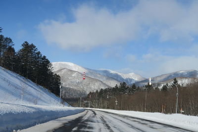 Snow covered road by trees against sky