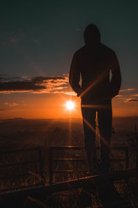 Rear view of silhouette man standing against orange sunset sky