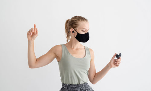 Music, isolation and leisure. young woman in a protective mask holding wireless earbuds and dancing