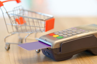 Close-up of credit card with machinery and miniature shopping cart on table