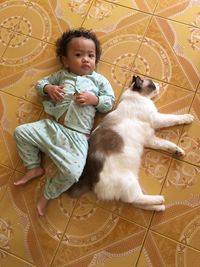 High angle portrait of baby girl lying with cat on tiled floor