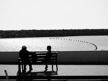 Silhouette people sitting on railing against sky