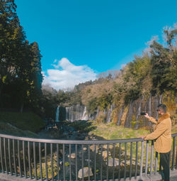 Man standing by railing against blue sky