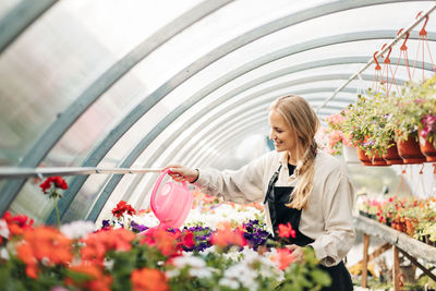 A smiling female gardener works in a greenhouse and enjoys hobbies, tending flowers. 