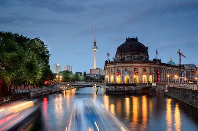 Illuminated bridge over river by buildings against sky in city