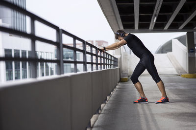 Side view of tired male athlete leaning on railing at parking lot