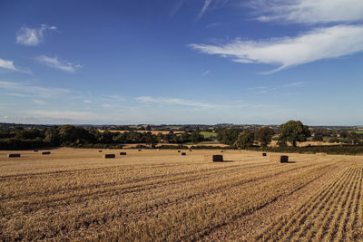 Hay bales on field against blue sky