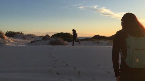 Rear view of people walking on road against sky during sunset