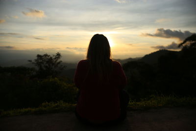 Silhouette woman sitting against sky during sunset