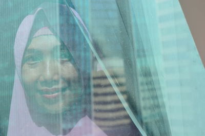 Portrait of woman wearing scarf seen through curtain