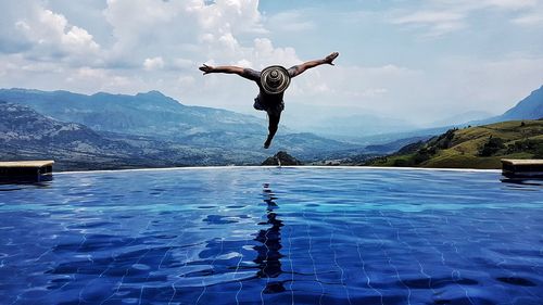 Man diving in swimming pool by mountains against sky