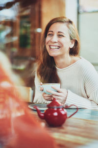 Portrait of smiling young woman using phone while sitting on table