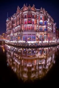 Illuminated building reflecting on lake at dusk