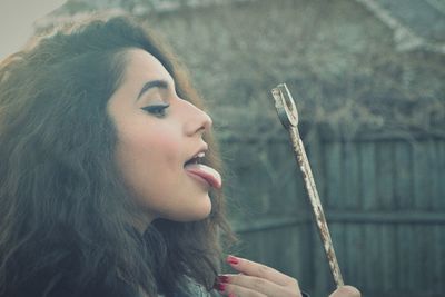 Side view of young woman with spanner sticking out tongue