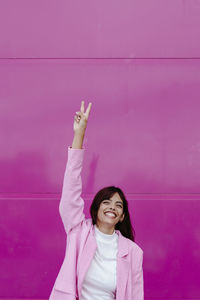 Portrait of smiling young woman standing against pink wall