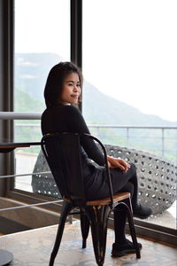 Side view of young woman looking away while sitting on chair against window in cafe